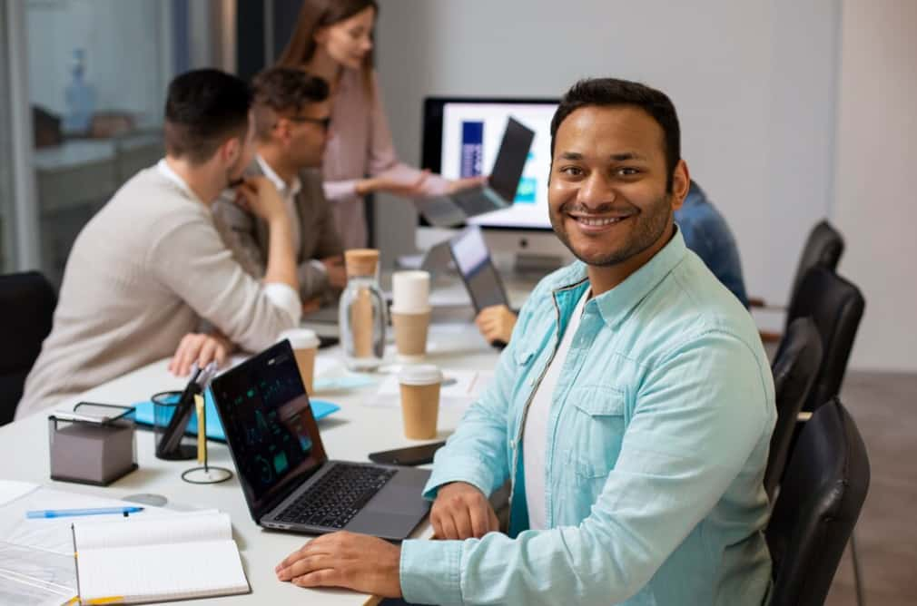 A smiling man at a meeting with colleagues in the background